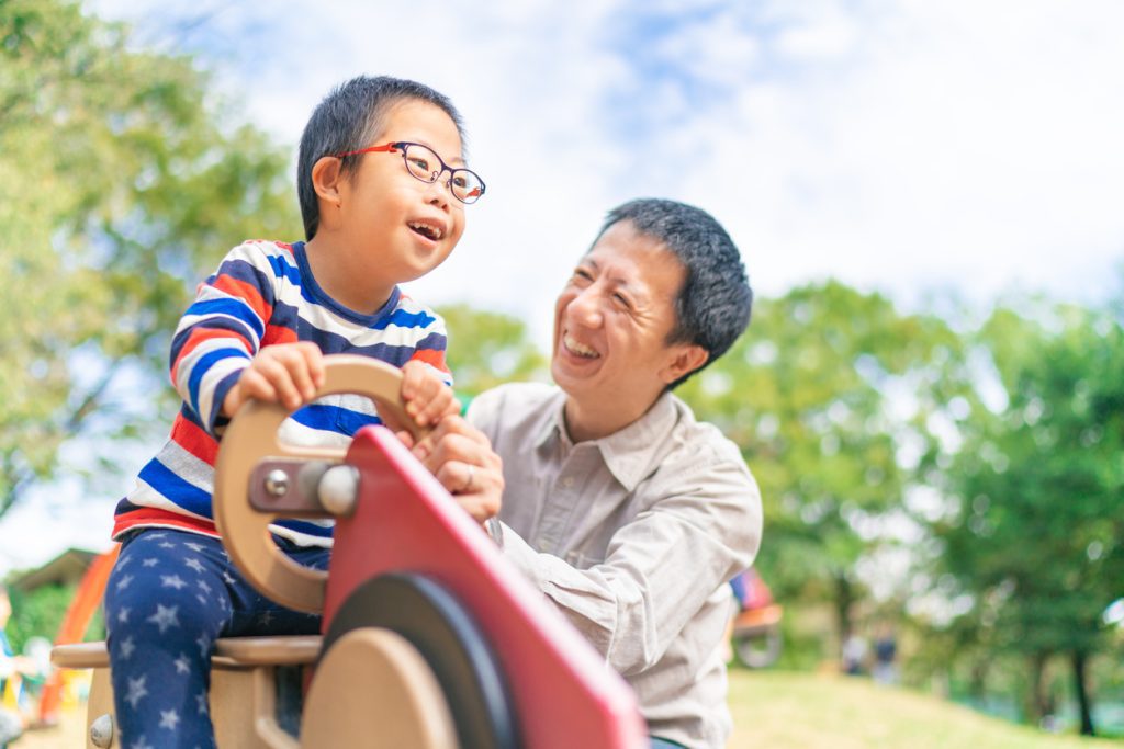Một đứa trẻ mắc hội chứng Down đang vui chơi với cha mình tại công viên công cộng vào một ngày nắng đẹp.